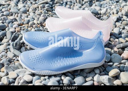 Ein Paar hellblaue und blassrosa Wasserschuhe zum Schwimmen auf einem felsigen Kieselstrand. Stockfoto