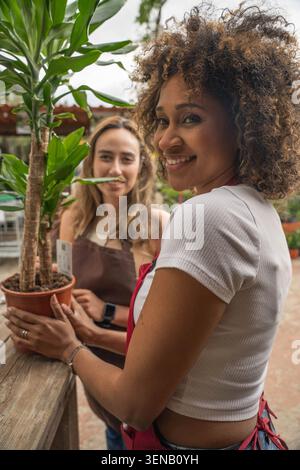 Lächelnder Blumenhändler, der im Gewächshaus eine Topfpflanze hält Stockfoto