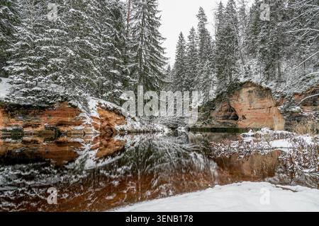 Sandsteinformationen aus schwarzen und weißen Klippen spiegeln sich im Winter im Fluss Brasla im Nationalpark Gauja in Lettland wider Stockfoto