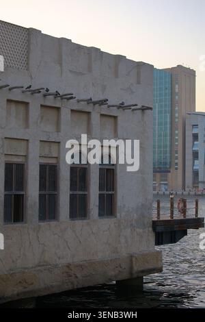 Traditionelle Architektur entlang einer Uferpromenade mit verwitterten Wänden und Holzbalken mit modernen Stadtgebäuden im Hintergrund. Stockfoto