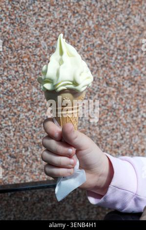 Die Hand eines Kindes, die eine Eiskugel auf einem Steingrund hält Stockfoto