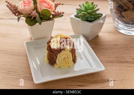 Blumenkuchen mit Buttercreme auf weißem Teller, in Stillleben geschossen. Natürliches Licht, Kuchen mit heller und dunkler Schokolade Zuckerguss. Konzept für Stockfoto