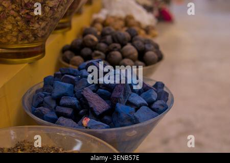 Lebendige Gewürze und getrocknete Blumen füllen Glasschalen. Blaue Würfel stehen im Kontrast zu Erdnüssen und Samen. Warme Beleuchtung hebt Texturen und Farben hervor. Stockfoto