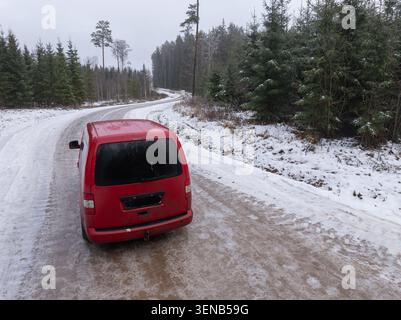 Roter Van auf vereister Waldstraße im Winter, Drohnenblick auf die ländliche Landschaft in Lettland Stockfoto