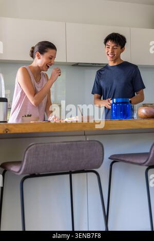 Diverse Paare, die lachen und Essen auf der modernen Kücheninsel zubereiten, mit Schneidebrett und Produkten Stockfoto