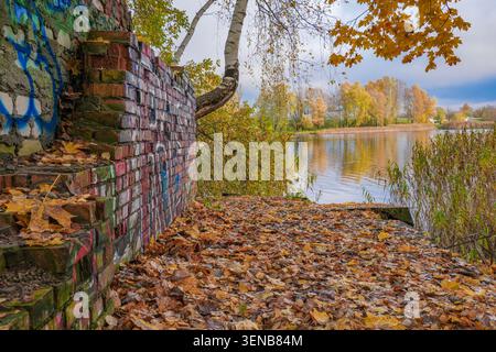 Graffiti-bedeckte Ziegelstruktur neben der herbstlichen Seeuferpromenade in Riga, Lettland Stockfoto