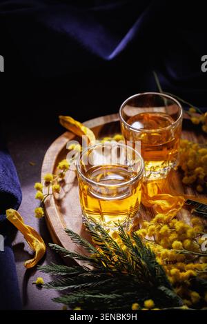 Whiskey oder Brandy Gläser mit Mimosa Blumen und Blütenblättern Frühlingsalkohol Stillleben Stockfoto