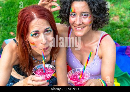 Zwei Frauen feiern das Pride Event und trinken Regenbogencocktails Stockfoto