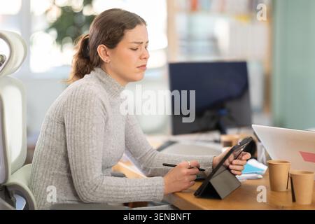 Traurige junge Frau, die im Büro am Computer arbeitet Stockfoto