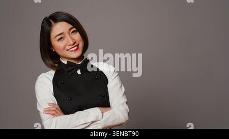 Mitarbeiter des asiatischen Restaurants servieren Kunden an Tischen, bieten luxuriöse Catering-Services mit Tablett auf der Kamera, Kellnerin in der Gourmet-Industrie, tragen Schürze und Bogen im Studio. Stockfoto
