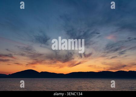 Der dramatische Sonnenuntergang zeigt den Himmel in lebendigen Farben über den Silhouetten der Berge im Südosten Alaskas. Stockfoto