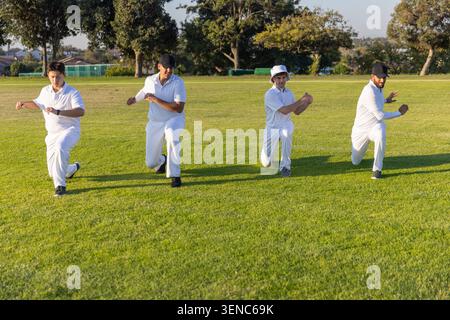 Verschiedene männliche Teamkollegen, die synchron Ausfallschritte auf grasbewachsenem Cricket-Boden in weißen Uniformen ausführen Stockfoto