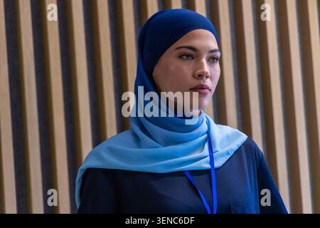 Afrikanische Frau, die vor einer hölzernen Lamellenwand steht, mit blauem Hijab, Schlüsselband und dunklem Oberteil Stockfoto