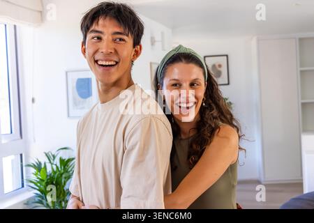 Diverse Paare lachen und umarmen in der Nähe eines großen Fensters im Wohnzimmer, Frau mit grünem Stirnband Stockfoto