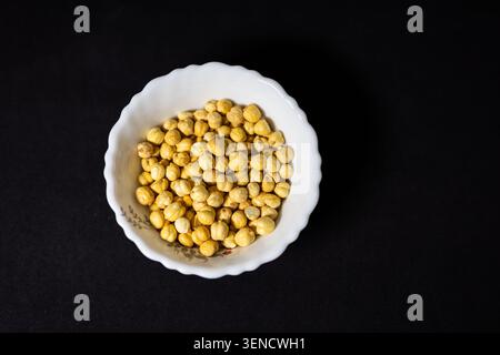 Proteinreiche geröstete Kichererbsen in weißer Keramikschale isoliert auf schwarzem Hintergrund Stockfoto