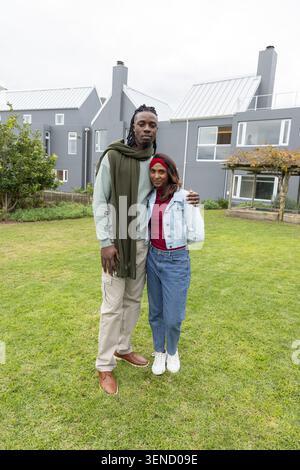 Diverse Paare stehen auf grasbewachsenem Rasen vor grauen Stadthäusern, Frau mit Jeansjacke Stockfoto