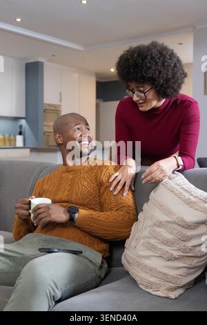 Verschiedene Paare sitzen auf grauem Sofa und plaudern, während ein Mann einen weißen Becher mit Smartphone auf dem Schoß hält Stockfoto
