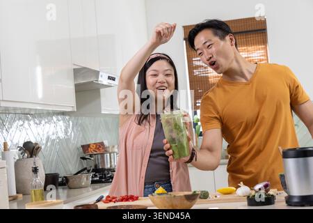 Verschiedene Paare bereiten grünen Smoothie in der Küche zu, halten Mixbecher und hacken Avocado Stockfoto