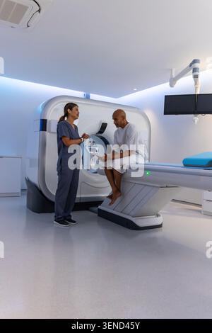 Afroamerikanischer Patient im Gewand, Techniker im Scrubs, der Tablette in der Bildgebung durch CT-Gantry hält Stockfoto