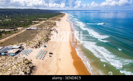 Costa Caparica, Lissabon. Blick aus der Vogelperspektive auf den Strand Costa Caparica, Portugal, mit goldenem Sand, türkisfarbenem Wasser und sanften Wellen. Üppige grüne Linien t Stockfoto