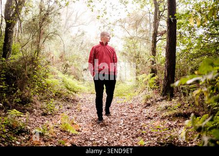 Mann in roter Jacke, der auf einem mit Blättern bedeckten Weg in einem Wald läuft Stockfoto