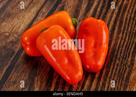 Drei leuchtende, orangefarbene, süße Paprika auf dunkler, strukturierter Holzoberfläche. Frisches Bio-Gemüse mit glänzenden grünen Stielen. Gesunde Ernährung Stockfoto