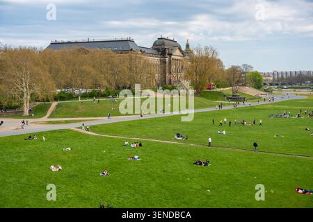 Dresden, Deutschland - 18. April 2026: Menschen, die sich auf einer grasbewachsenen Flusswiese entlang der Elbe in Dresden entspannen. Freizeit und Freizeit im Freien Stockfoto
