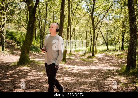 Mann genießt Natur spazieren im Wald, während er Audio über Kopfhörer hört Stockfoto