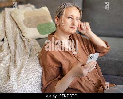Frau, die beim Surfen im Internet ein Smartphone mit zweifelhaftem Ausdruck verwendet. Unsicherheit, Zögern und Entscheidungsprozesse im digitalen Alltag. Stockfoto