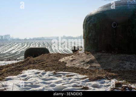 Deutsche Panzerbunkerkuppel aus Stahl des Zweiten Weltkriegs auf einem Hügel mit schmelzendem Schnee und einem gepflügten landwirtschaftlichen Feld im Hintergrund, Wintersaison, Polen Stockfoto