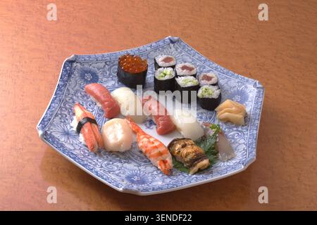 Auf einem dekorativen Teller steht eine abwechslungsreiche und kunstvoll angeordnete Platte mit Sushi- und Maki-Rollen. Die lebendigen Farben und Texturen der frischen Meeresfrüchte und r Stockfoto