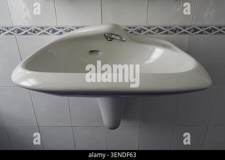 Weißes keramikbeschichtetes Wand-Waschbecken mit Chrom-Wasserhahn, geflieste Wandinnenseite Nahaufnahme Stockfoto
