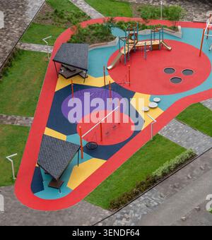 Blick aus der Vogelperspektive auf den farbenfrohen, modernen Kinderspielplatz mit Schaukeln, Rutschen, Kletterstrukturen und Sicherheitsgummiböden im angelegten Wohnbereich Stockfoto