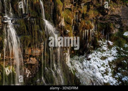 Wasserfall, der im Winter über moosige Felswände stürzt, mit Eiszapfen und Schnee in den Yorkshire Dales Stockfoto