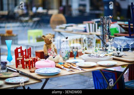 Vintage-Geschirr, Glaswaren, kleine Möbel, Spielzeug und Sammlerstücke, die auf einem Tisch auf einem Flohmarkt in Frankreich ausgestellt werden, mit Abbildungen von Secondhand-Shopping, Stockfoto
