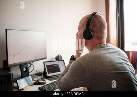Anleger mit Kopfhörern, die sich auf Finanzdiagramme konzentrieren, die auf mehreren Bildschirmen angezeigt werden Stockfoto