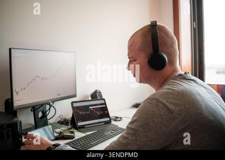 Mann überwacht Börsendiagramme und Kryptowährungstrends auf Computern, Tablets und Telefonen Stockfoto