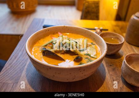 Authentische scharfe Laksa-Nudelsuppe mit frischem Gemüse in gemütlicher Restaurantatmosphäre Stockfoto
