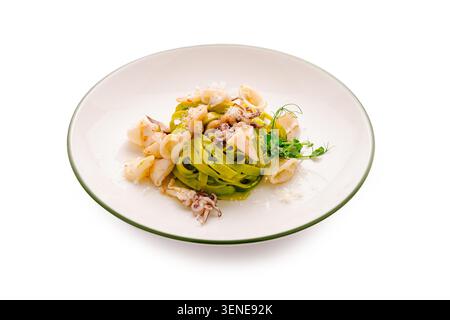 Auf einem Teller finden Sie grüne Nudeln, die mit kleinen Meeresfrüchten belegt sind. Frische Kräuter werden zur Dekoration darauf gelegt. Die Umgebung sieht aus wie ein Restaurant. Stockfoto