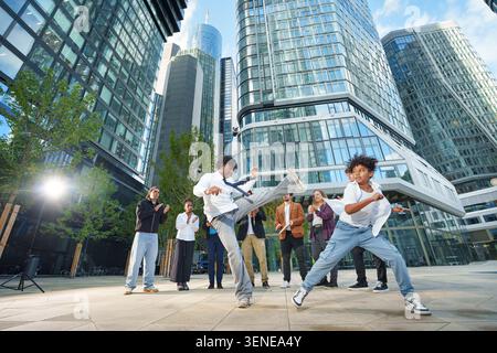 Eine Gruppe sportlicher Menschen unterschiedlichen Alters in Business-Outfits trainiert Capoeira in einer Großstadt Stockfoto