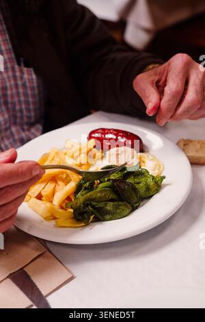 Mann isst traditionelle spanische Teller Chorizo, Spiegelei, Padron Paprika und Pommes frites im Restaurant. Spanische Gastronomie. Stockfoto