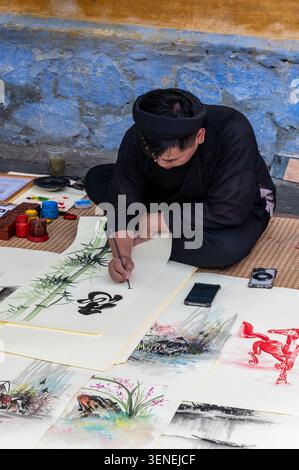 Ein vietnamesischer Schriftsteller/Künstler, der traditionelle Kalligraphie verwendet, indem er einen spitzen Stift verwendet, der mit schwarzer indischer Tinte beschichtet ist und verschiedene Strichbreiten durchzieht Stockfoto