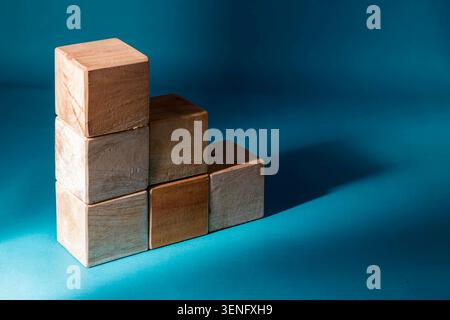 Sechs Holzwürfel in Stufen- oder Treppenform vor tiefblauem Hintergrund mit scharfer Beleuchtung und langen Schatten, die den beruflichen Aufstieg oder das finanzielle Wachstum konzeptualisieren. Stockfoto