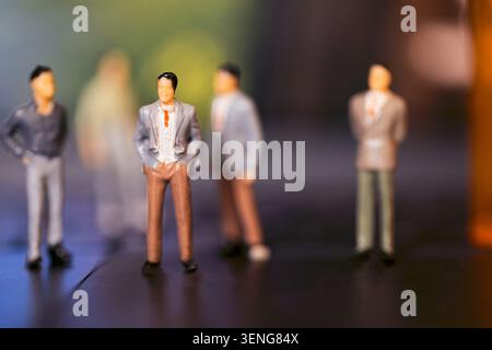 Kleine Geschäftsfiguren in Anzügen sind auf einer schwarzen Oberfläche positioniert, mit einem unscharfen Hintergrund, der Tiefe und Konzentration auf die Motive schafft Stockfoto
