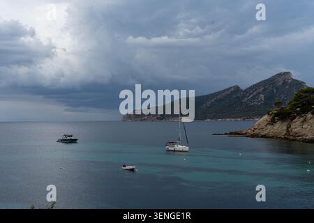 Sturmwolken über der ruhigen Bucht mit verankertem Segelboot und türkisfarbenem Wasser Stockfoto