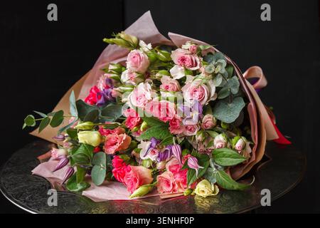 Gemischter rosa Strauß in Kraftpapier auf silbernem Tablett, Rosen, Eukalyptus und Nelken, schwarzer Hintergrund, Floristengeschenk Stockfoto
