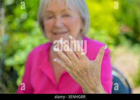 Nahaufnahme einer eleganten Seniorin, die ihre gepflegte Hand im Freien in einem grünen Sommergarten präsentiert. Lifestyle-Konzept für anmutiges Altern, bea Stockfoto