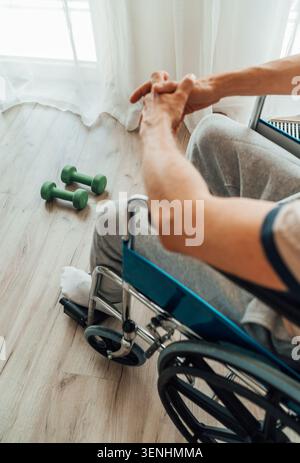 Nahansicht eines Mannes im Rollstuhl in einem hellen Raum mit grünen Hanteln auf dem Boden, die das Motto der adaptiven Fitness-Physiotherapie darstellen Stockfoto