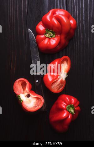 Rote Paprika mit geschnittenen Stücken auf dunklem Hintergrund. Frischer süßer Pfeffer, gesunde Kochzutat Stockfoto
