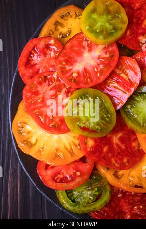 Nahaufnahme farbenfroher Tomatenscheiben im Kreis. Vegetarische Bio-Zutaten, lebendige Essenstextur Stockfoto
